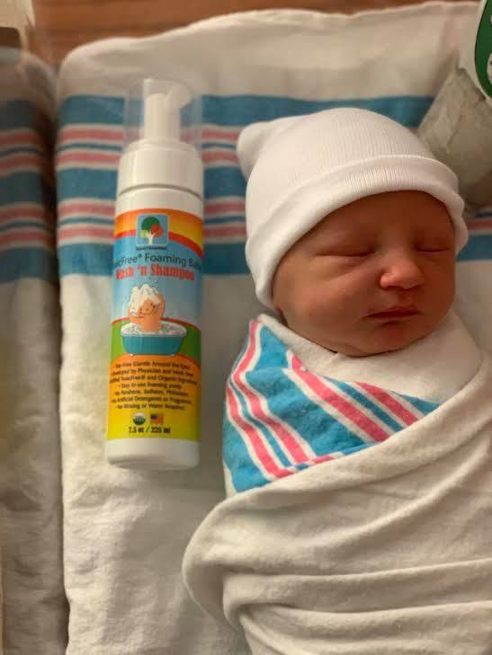 bottle of Raise Them Well's certified toxic-free foaming baby wash and shampoo laying next to swaddled newborn in layette